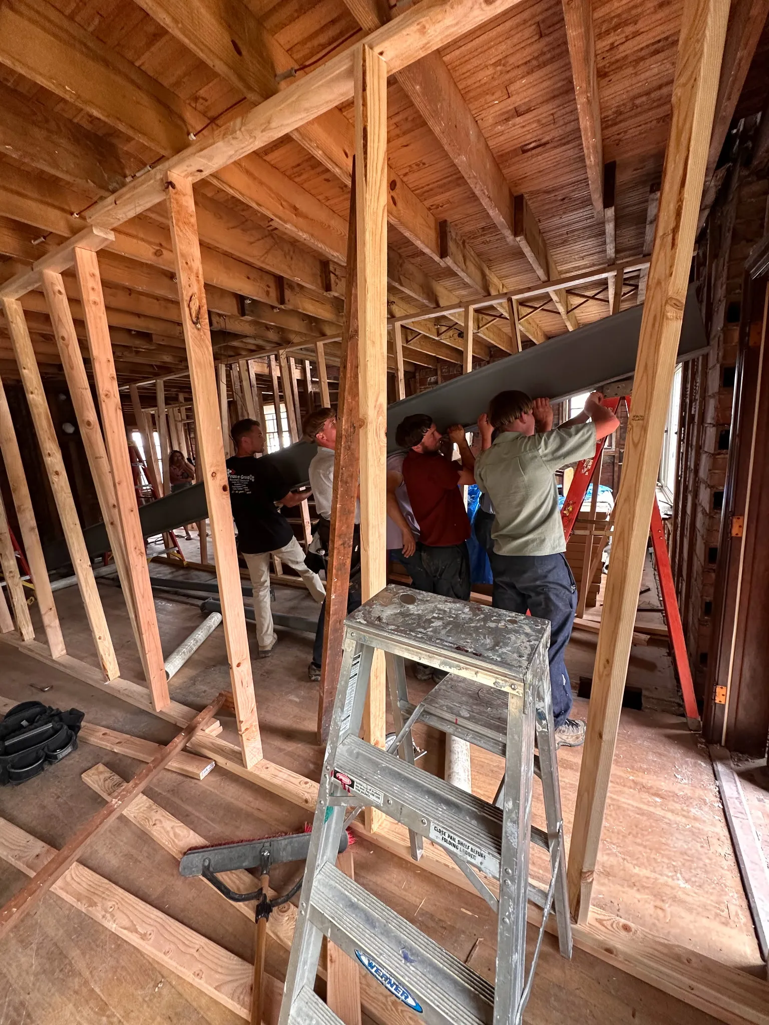 Multiple crew members lifting and installing a steel beam inside framed walls