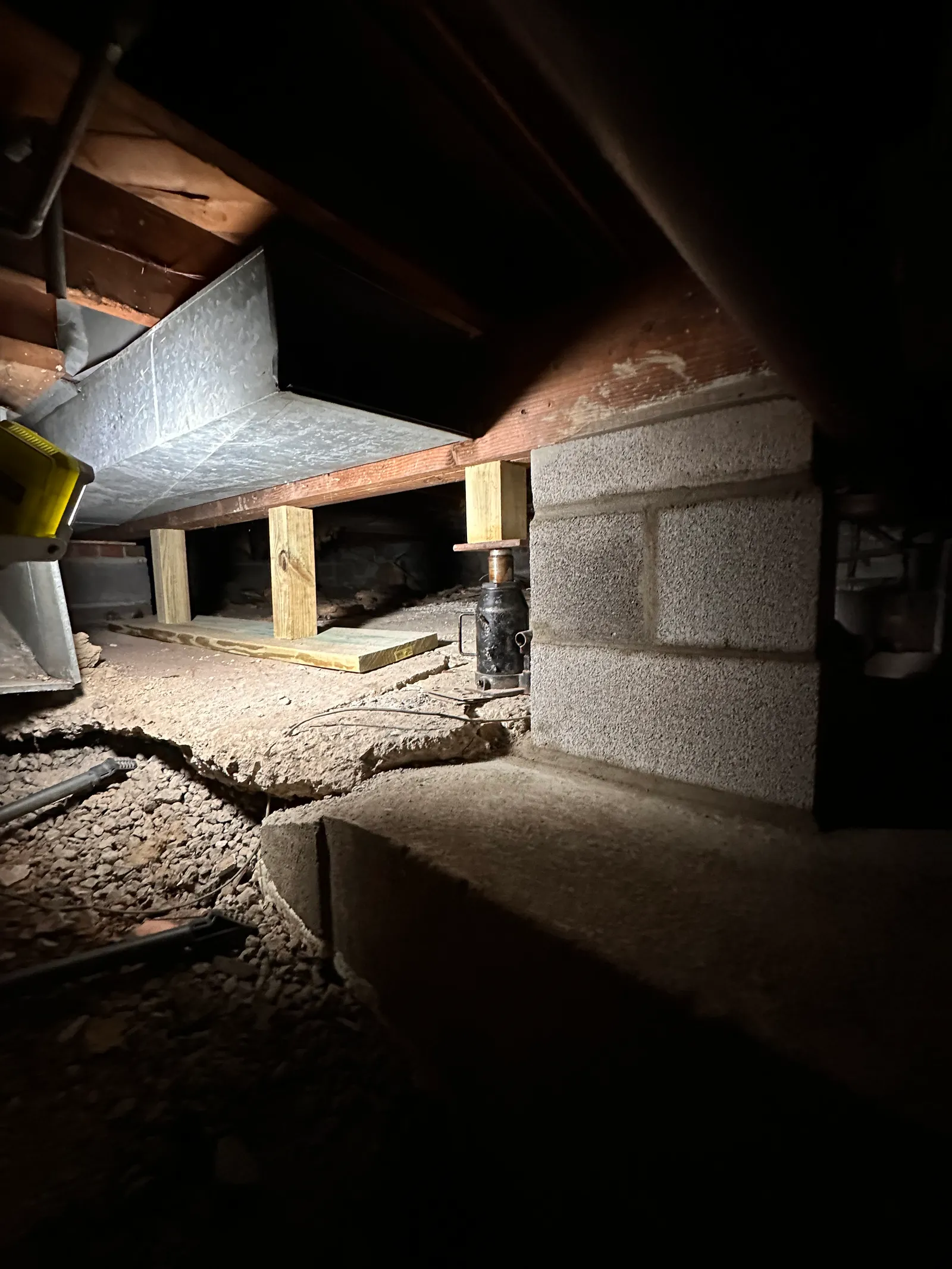 Adjustable jack post supporting wood beam beneath floor joists in crawlspace