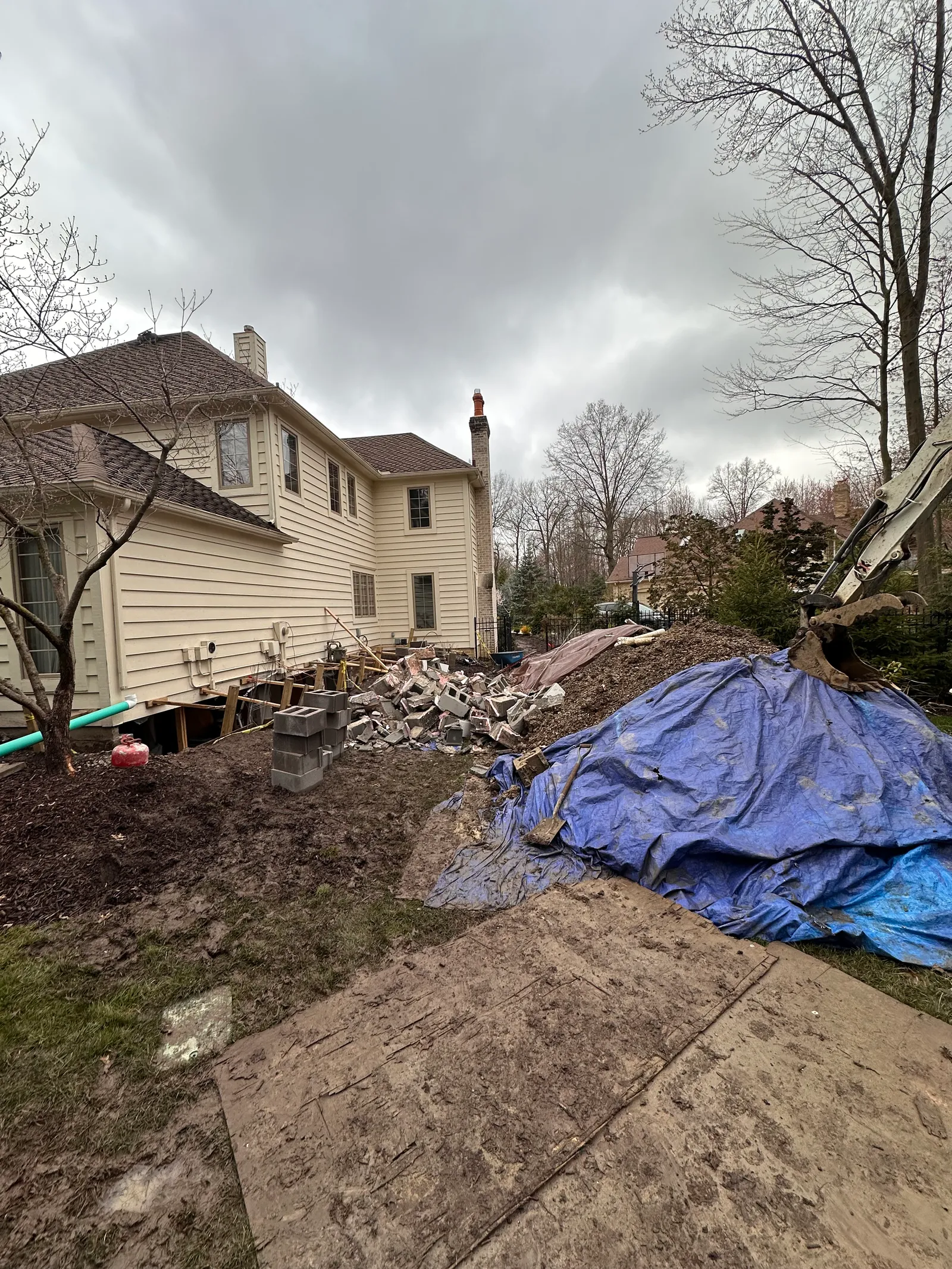 Residential exterior with blue tarp protecting active foundation repair zone