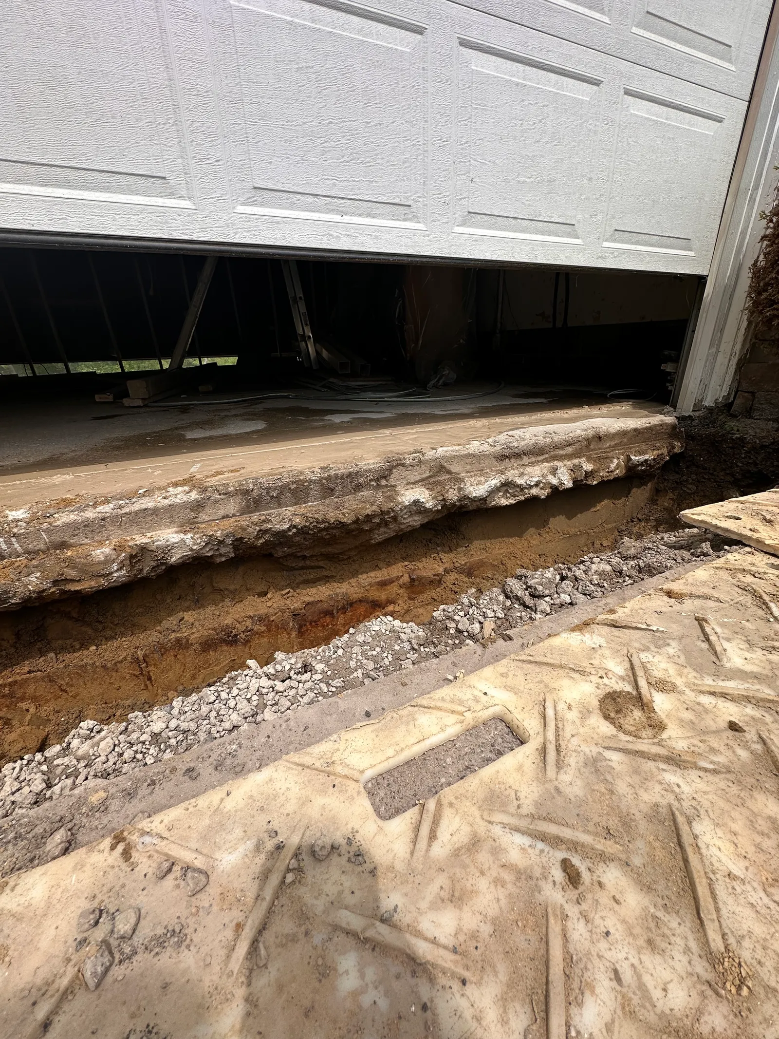 Foundation excavation near garage door revealing footing and soil layers