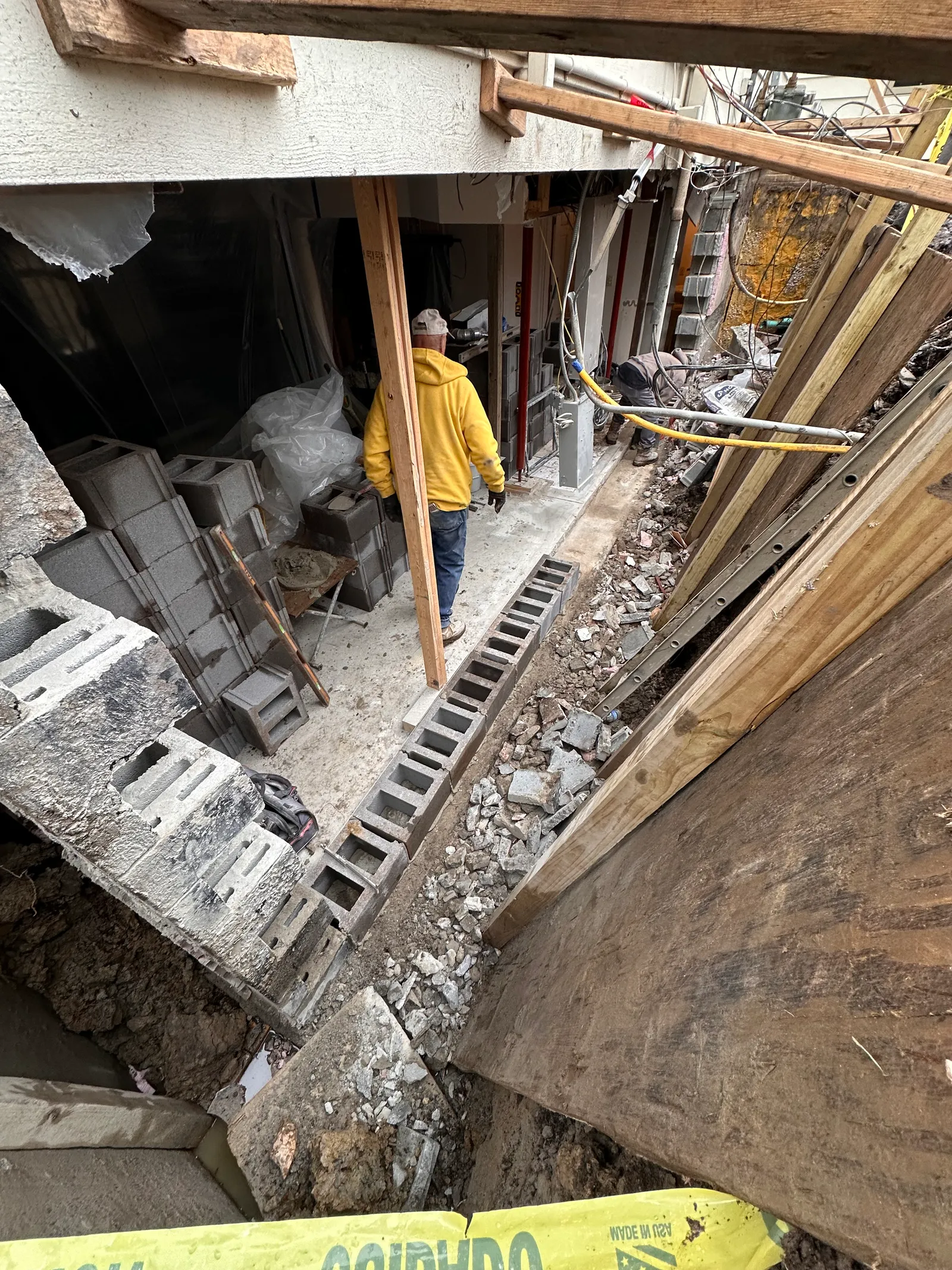 Worker in excavated trench alongside exposed CMU block foundation wall